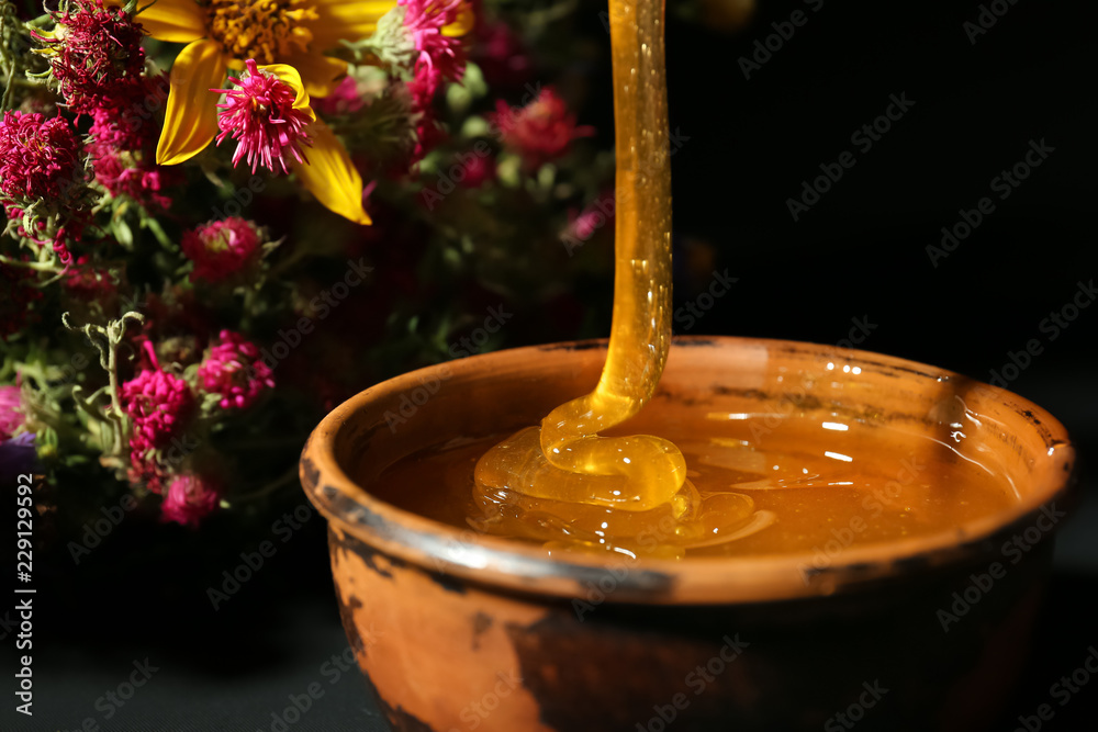 Honey pouring in bowl on dark background