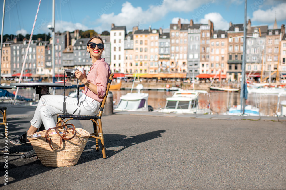 Young woman enjoying coffee sitting at the cafe outdoors near the harbour with beautiful buildings o