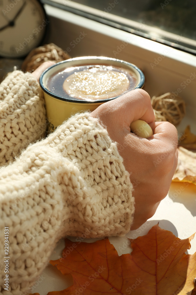 Woman holding cup of aromatic tea on windowsill