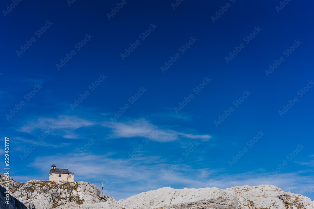 Mountain chapel or church built on the rock. High alpine landscape, blue sky, rocks and rock walls. 