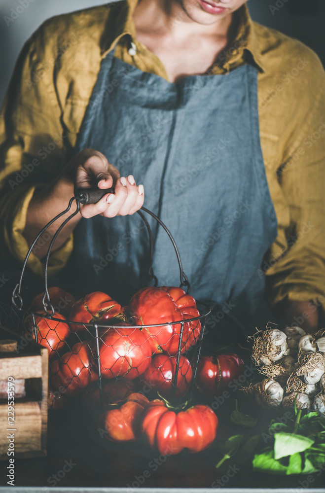 Woman in linen apron holding basket with ripe heirloom tomatoes for cooking tomato sauce, canned tom