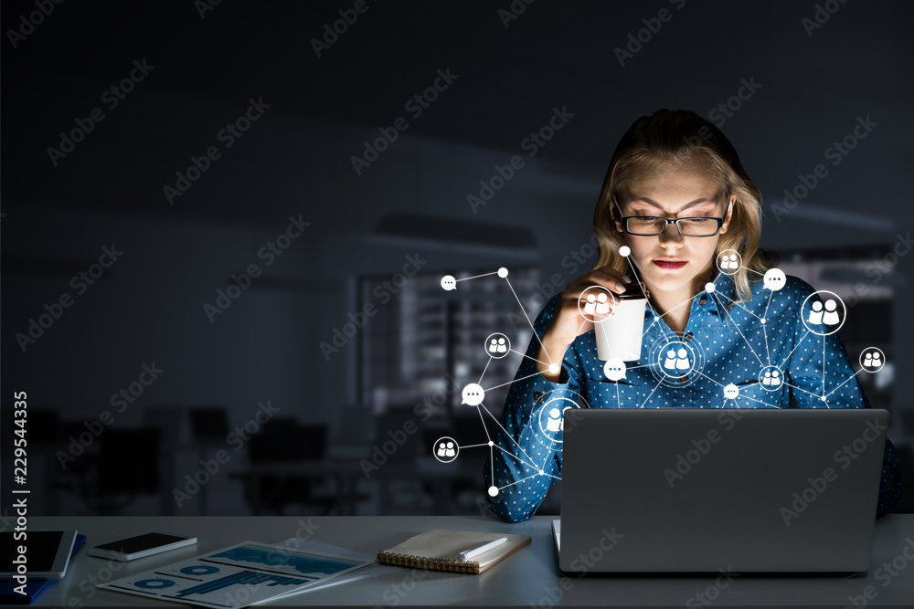 Attractive blonde wearing glasses in dark office using laptop. Mixed media