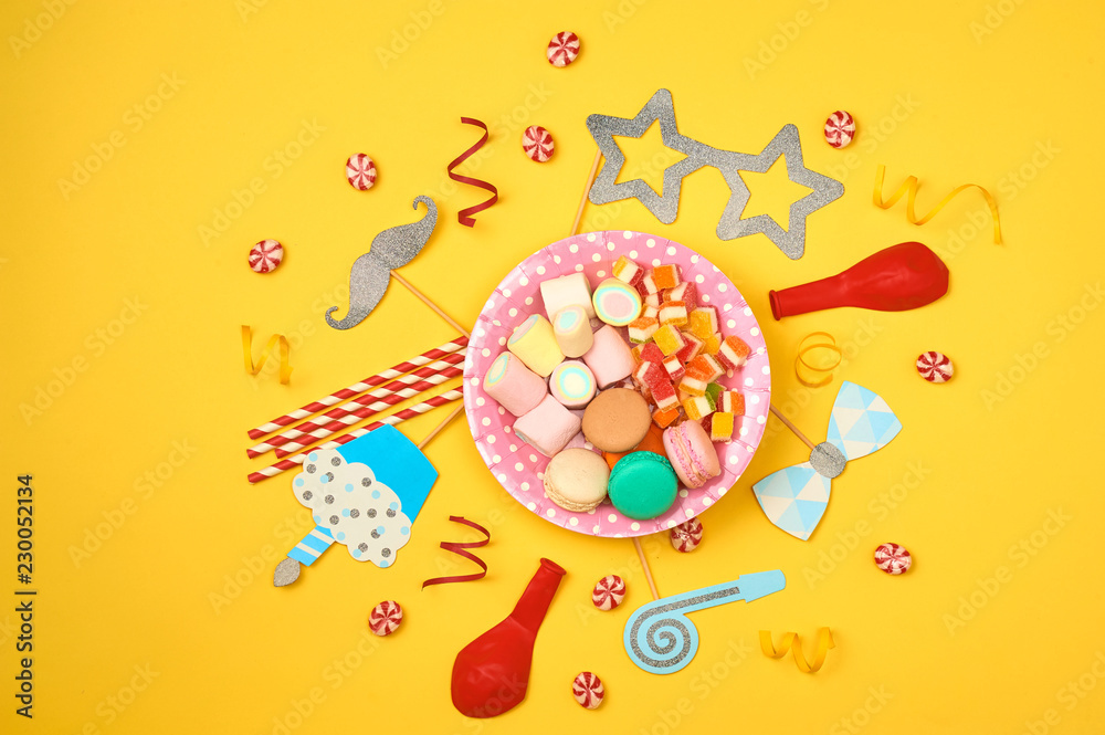 Colored party, sweets and confetti on yellow background top view mockup