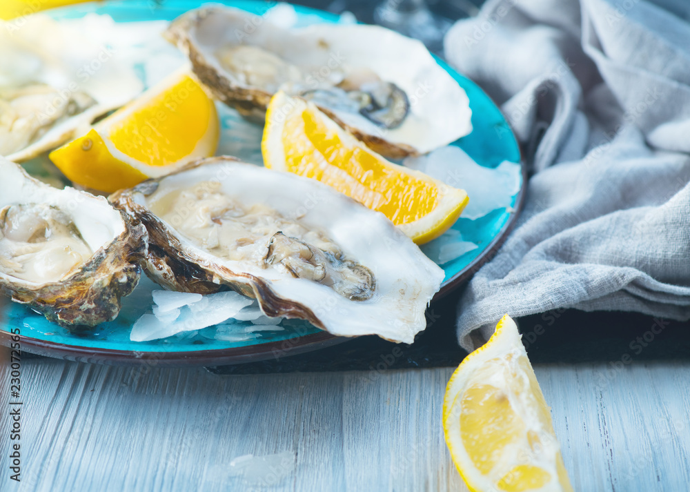 Fresh Oysters closeup on blue plate, served table with oysters, lemon and ice. Healthy sea food. Oys