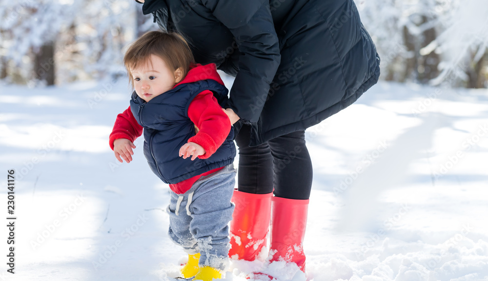 Toddler boy playing in the snow with his mother