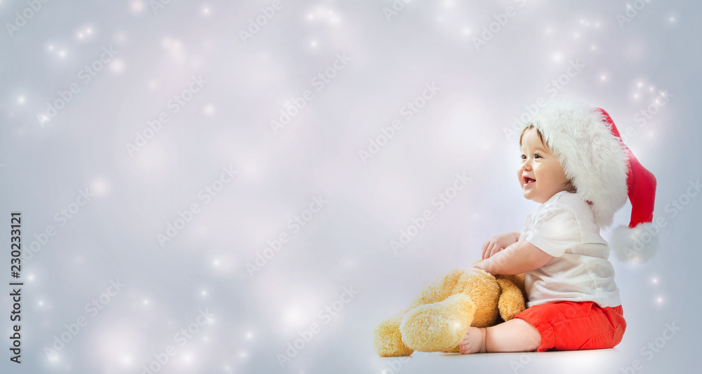 Toddler boy with santa hat playing with his teddy bear in snowy day