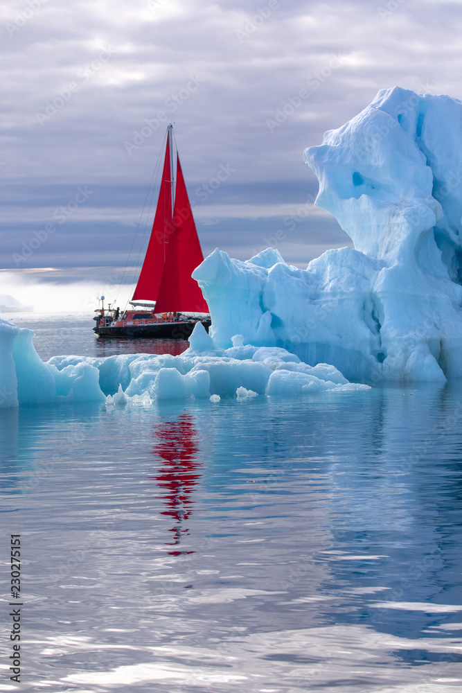 北极美丽的红色帆船，旁边是一座巨大的冰山，展示了其规模。Ilulissat，Disko B