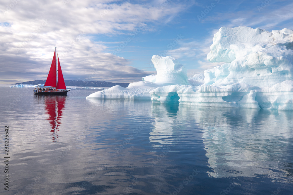 北极美丽的红色帆船，旁边是一座巨大的冰山，展示了其规模。Ilulissat，Disko B