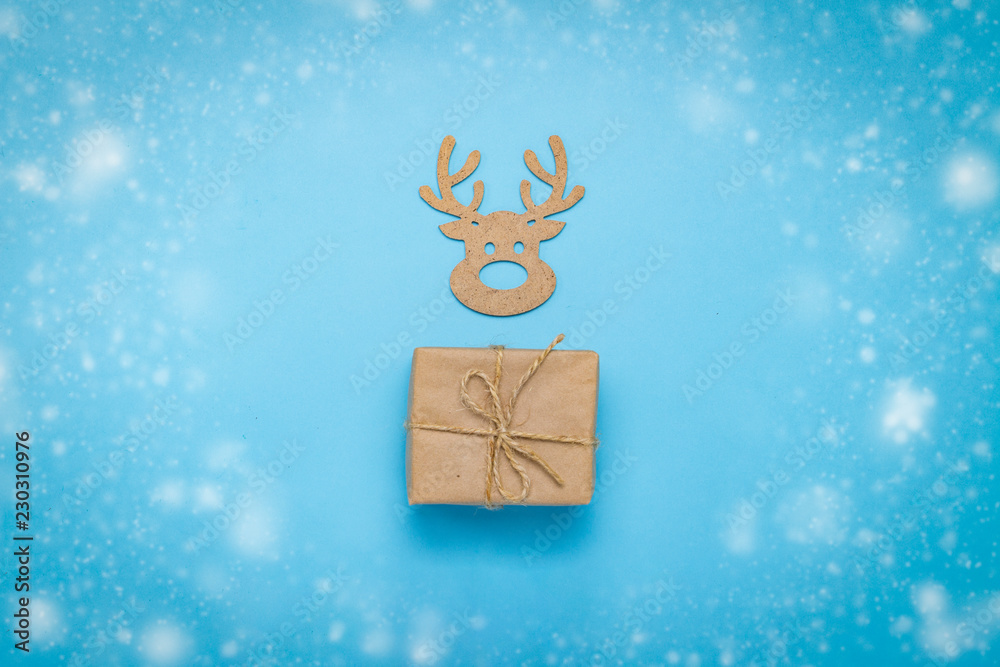 Gift box and Christmas wooden toy Deer head on a blue background with the effect of falling snow. Co