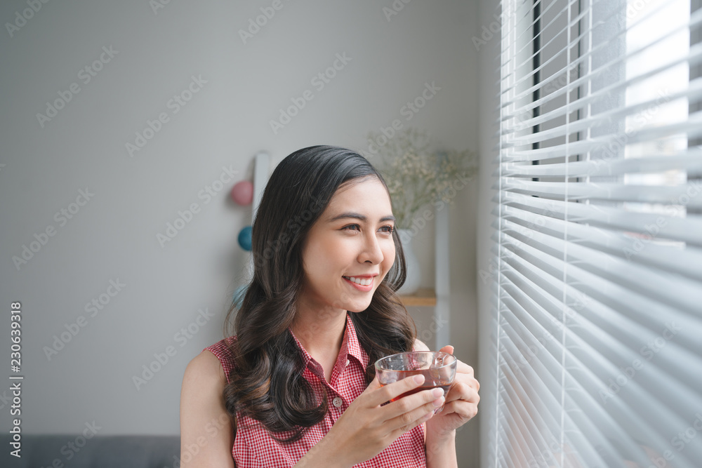 微笑的年轻女性在家工作或学习时喝咖啡或茶。