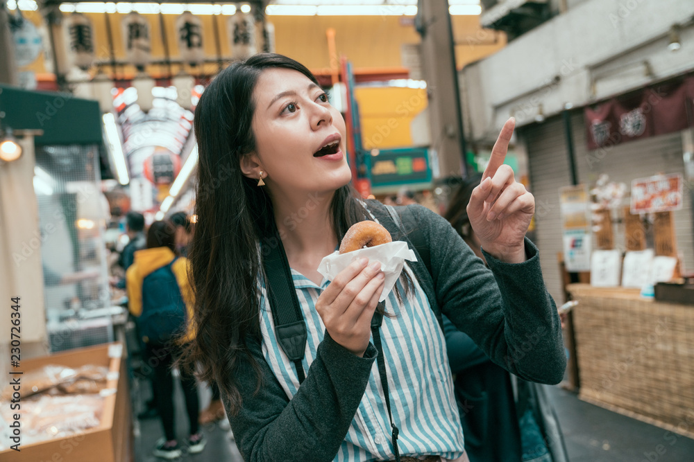 游客指着小贩，手里拿着甜甜圈。