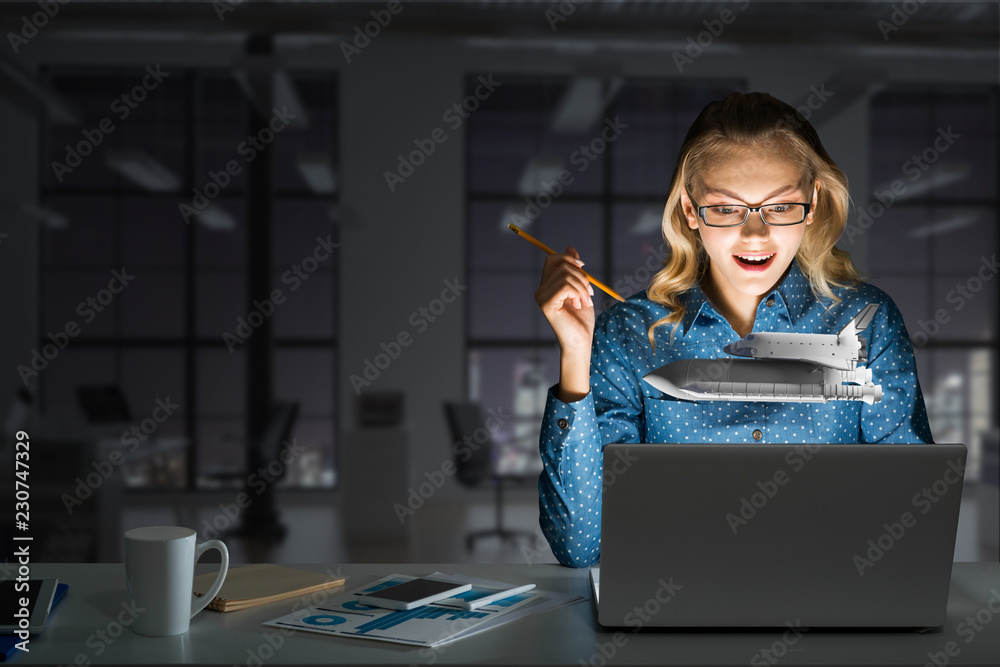 Attractive blonde wearing glasses in dark office using laptop. Mixed media