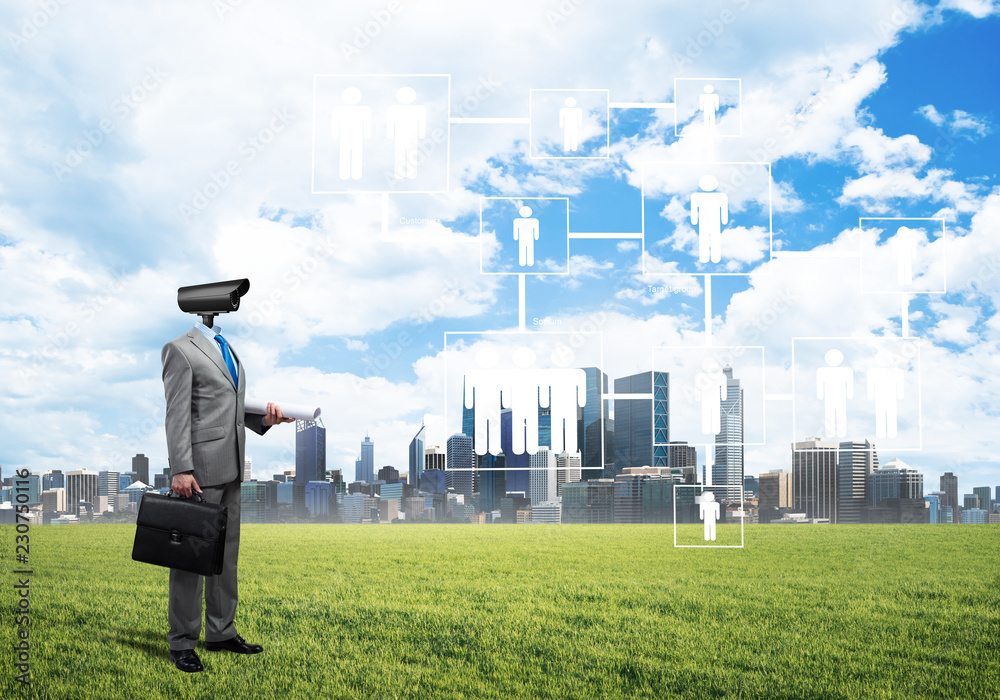 Camera headed man standing on green grass against modern cityscape