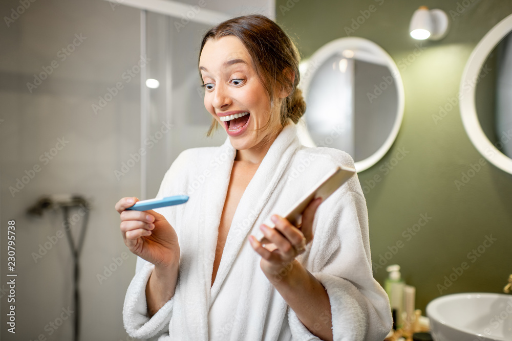 Happy woman in bathrobe excited with a pregnancy test result in the bathroom