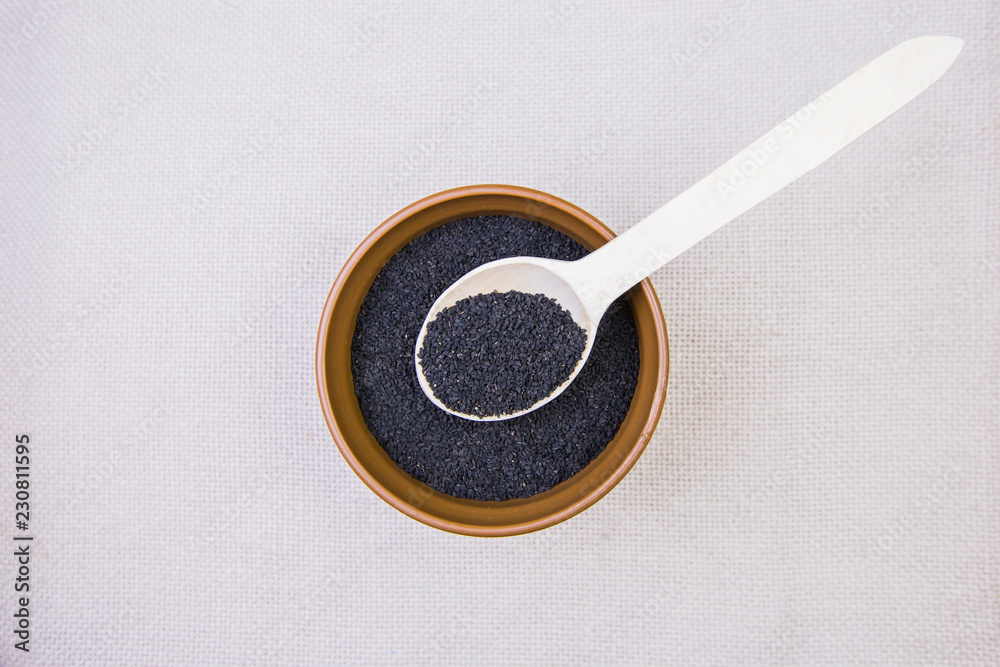 Black cumin in a plate with a wooden spoon on a light burlap background