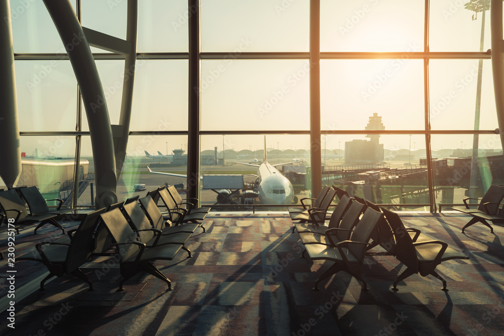 Empty chairs in the departure hall at airport with airplane taking off at sunset. Travel and transpo