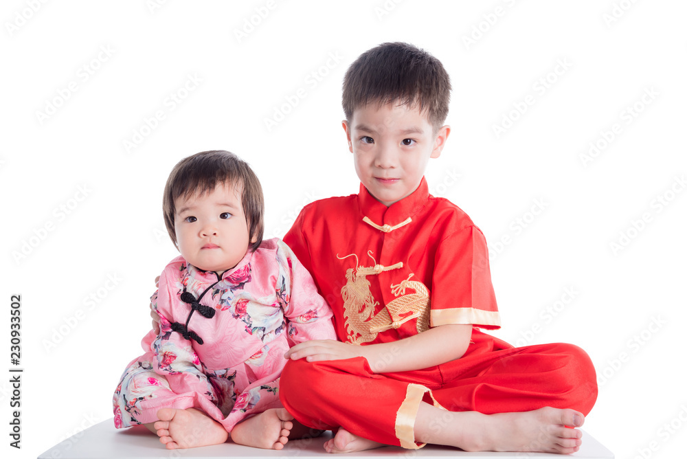 Two chinese children wearing traditional costume sitting on table over white background