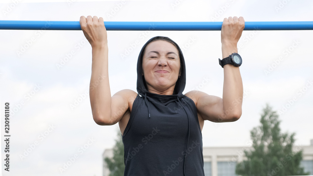 Fitness woman workout tries doing exercises on a horizontal bar outdoors