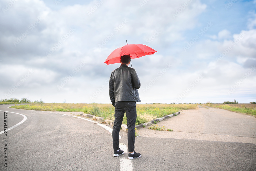 撑着雨伞的年轻人站在十字路口。选择的概念