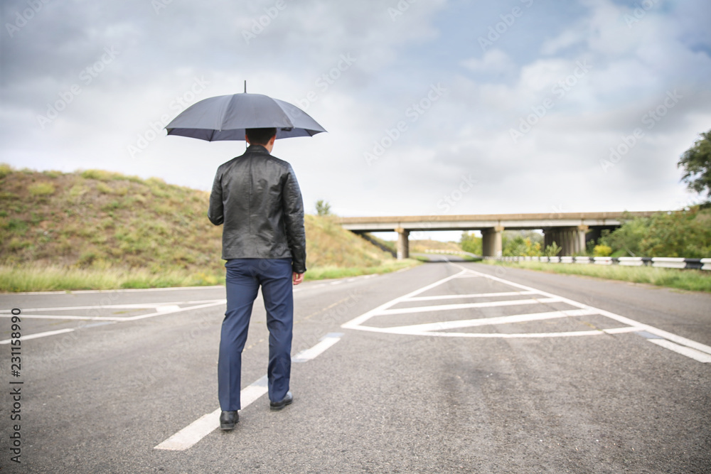 Young man with umbrella going along road. Concept of choice