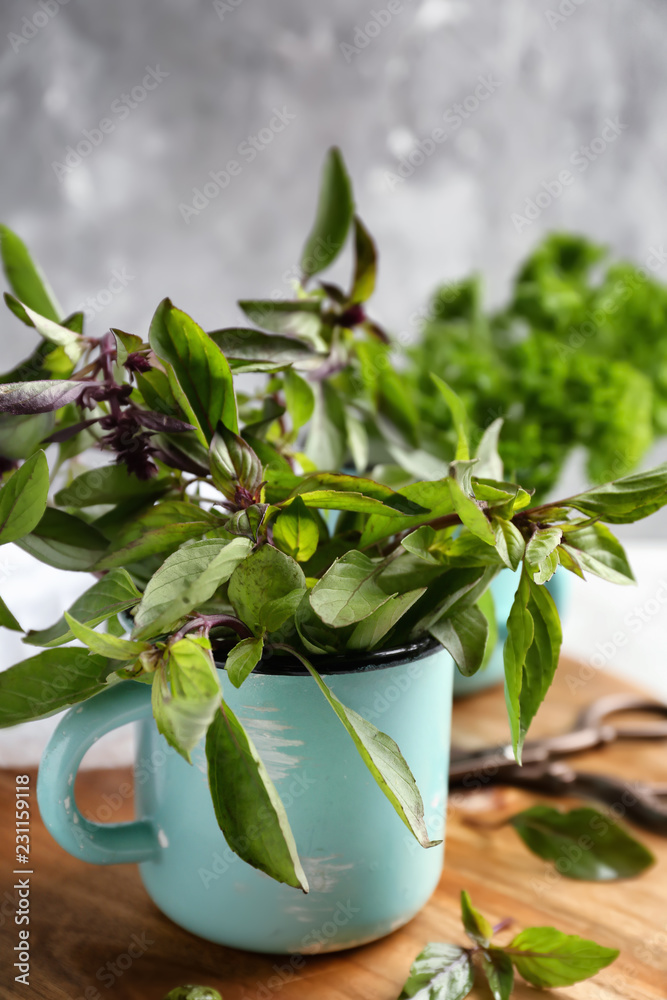 Metal cup with fresh aromatic basil on wooden board