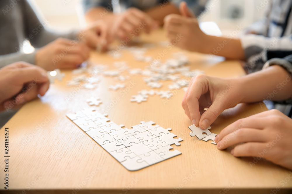 Group of people assembling puzzle on wooden table