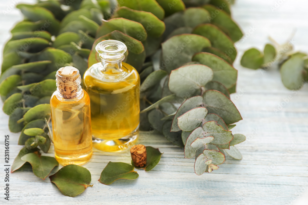 Bottles with essential oil and eucalyptus branches on wooden table