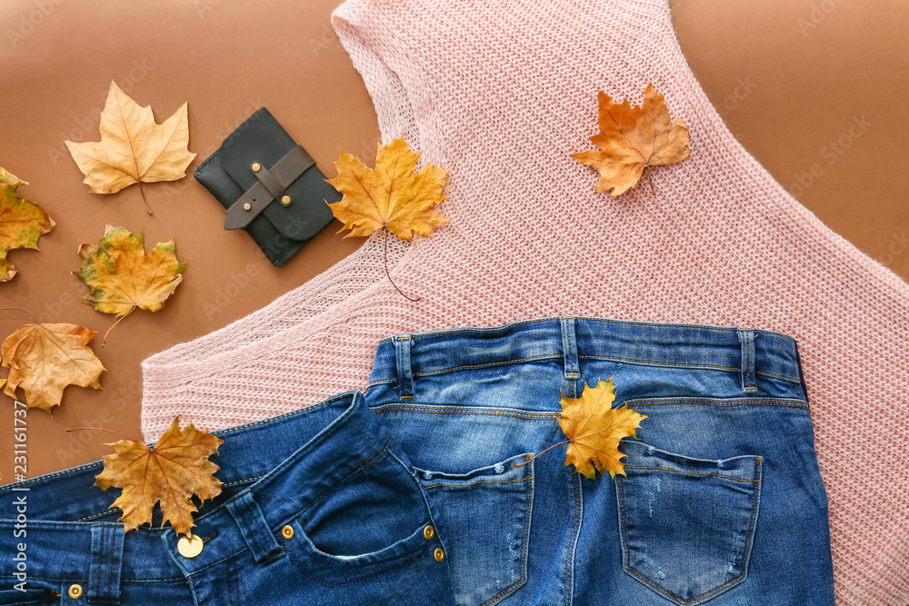 Stylish outfit with wallet and autumn leaves on color background, top view