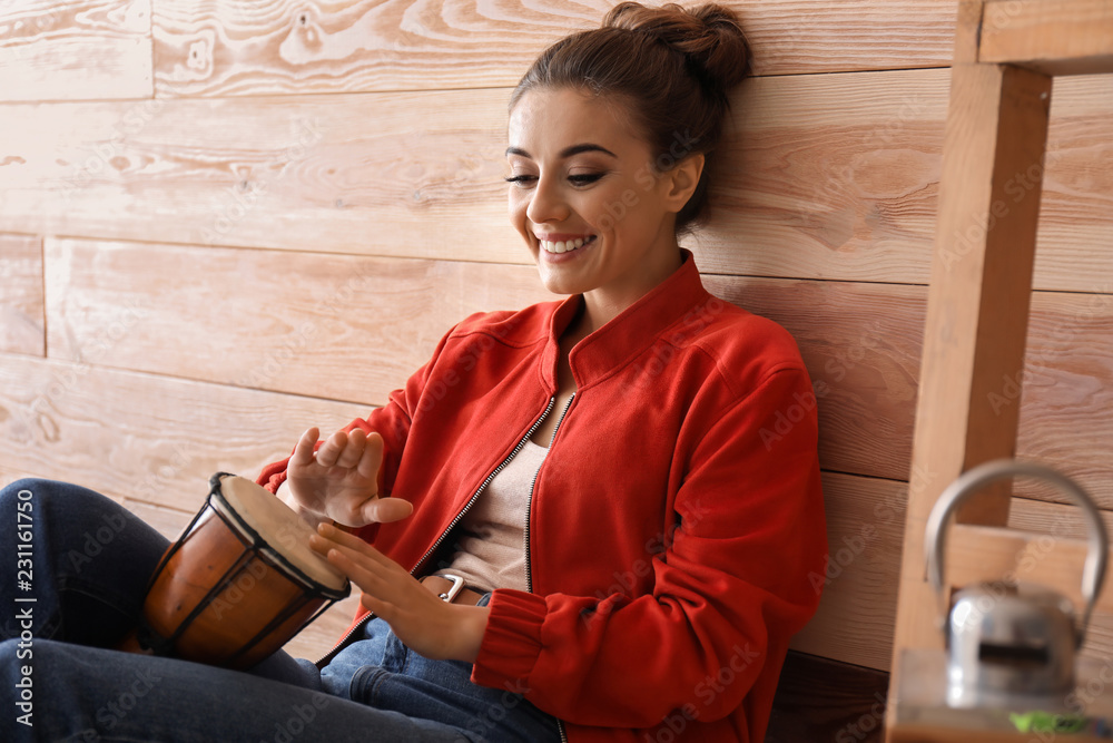 Beautiful woman playing tam-tam near wooden wall