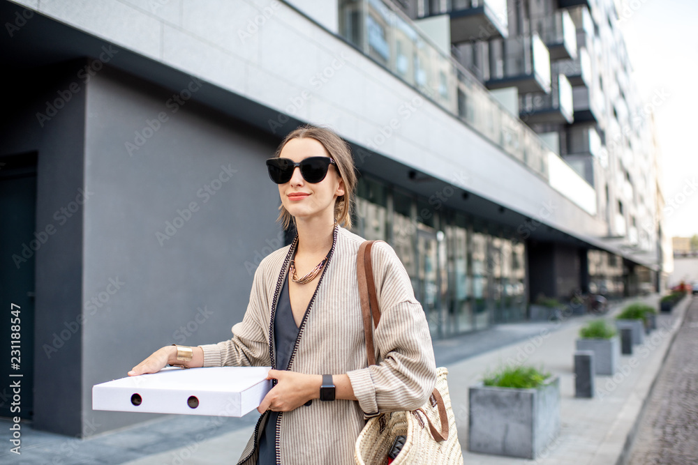 Young stylish woman walking with pizza box outdoors at the modern residential area