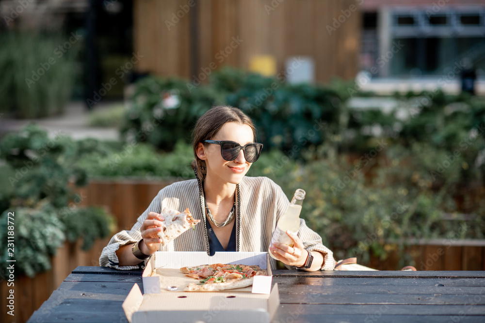 一名年轻女子坐在现代公园的户外吃披萨零食