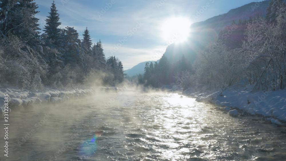 LENS FLARE Mist rolling over the mountain stream flowing through snowy landscape