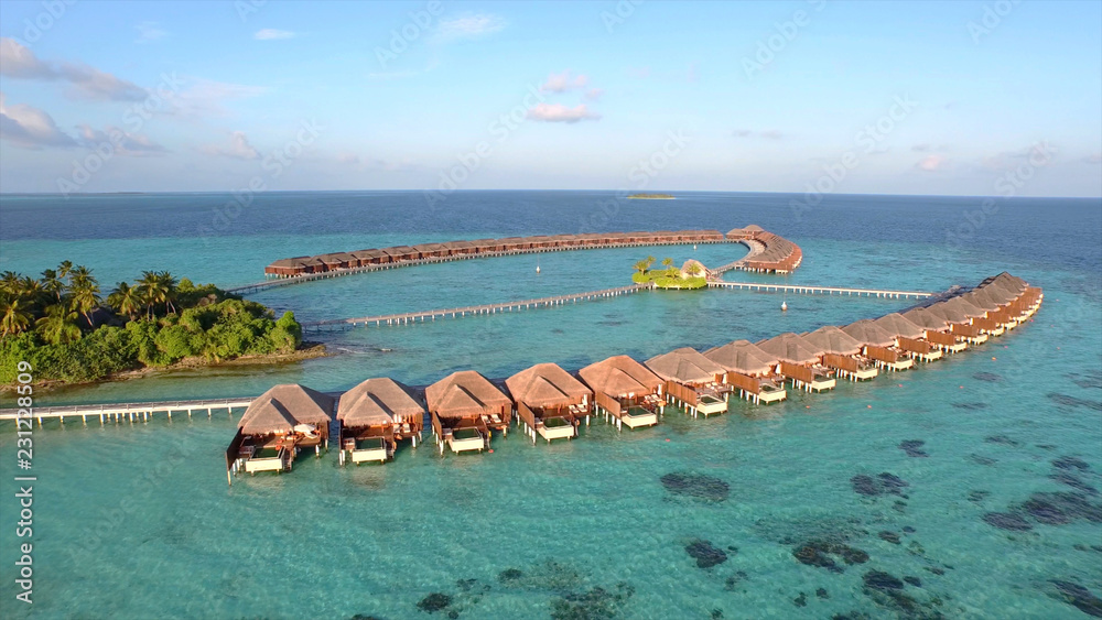 AERIAL: Flying towards wooden huts built above the crystal clear ocean water.