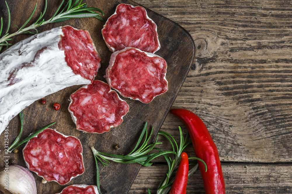 Sliced salami with spices, chili pepper and rosemary on wooden cutting board over rustic table. top 