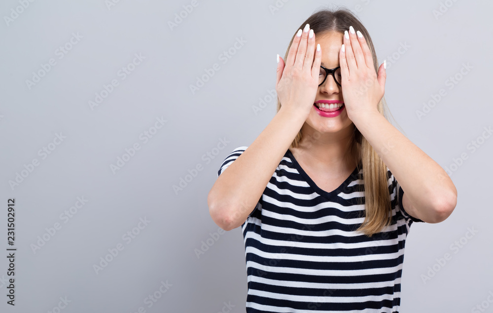 Young woman covering her eyes with her hands on a gray background