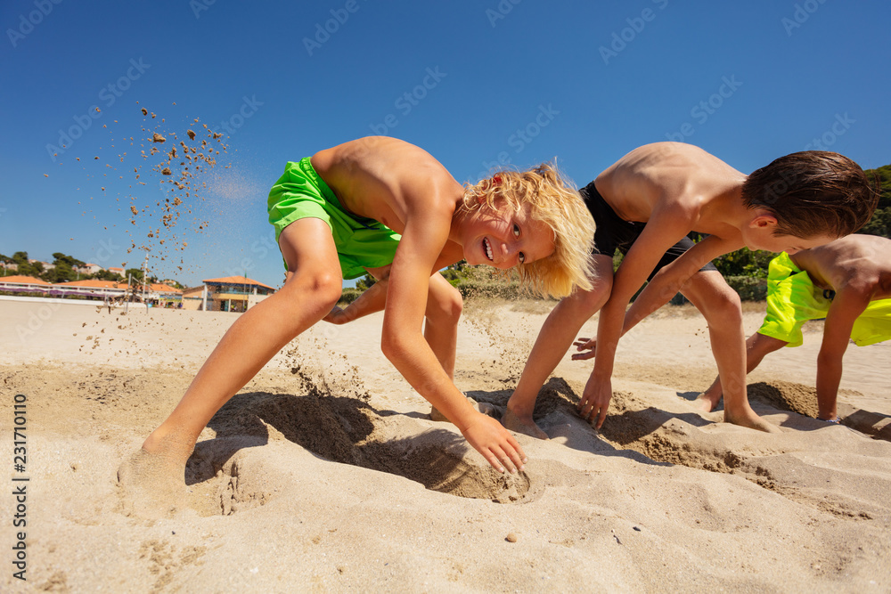 Cute boy digging holes with friends on sandy beach