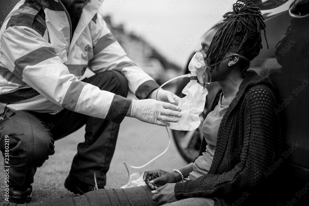 Male paramedic putting on an oxygen mask to an injured woman on a road