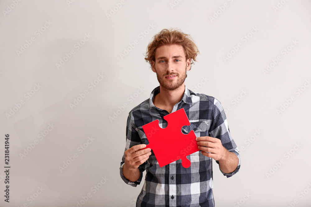 Young man with piece of jigsaw puzzle on light background