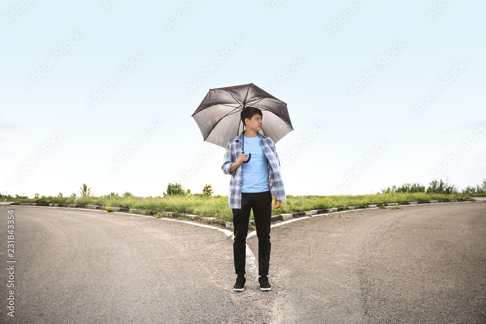 撑着雨伞的年轻人站在十字路口。选择的概念