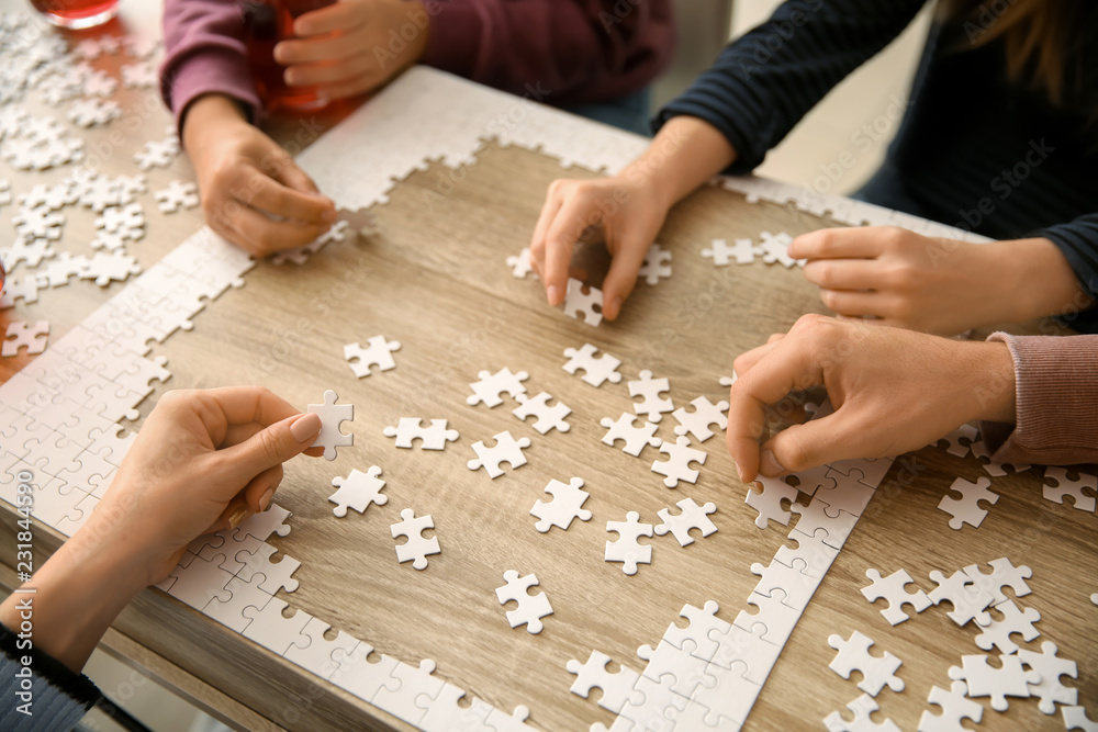 Group of people assembling puzzle on wooden table