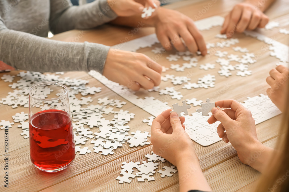 Group of people assembling puzzle on wooden table