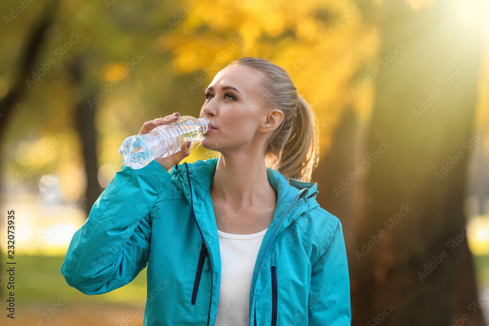 Sporty young woman drinking water in autumn park