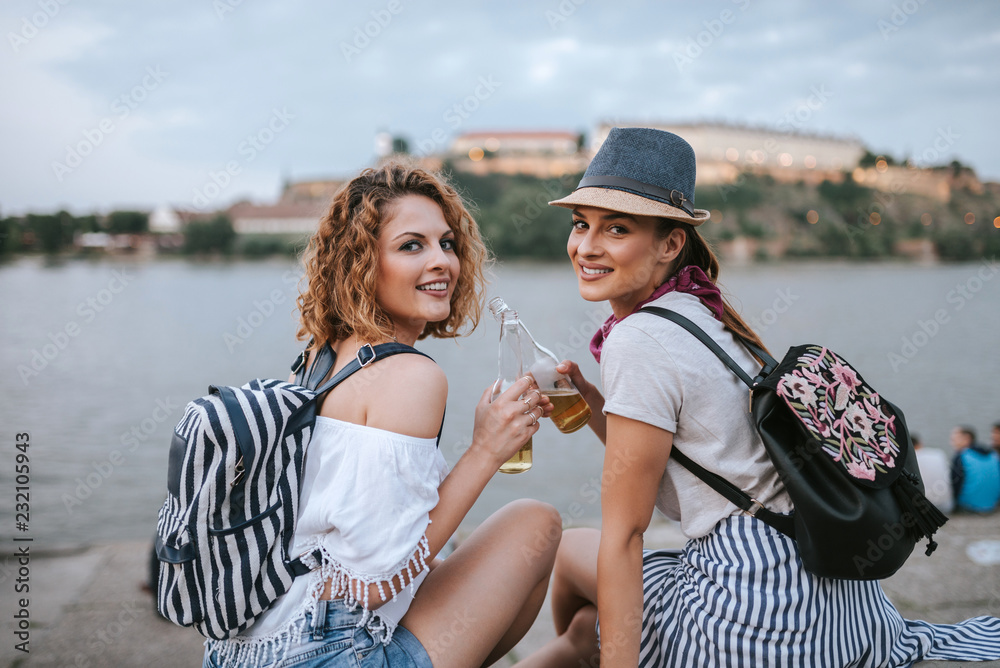 Two gorgeous girls toasting while sitting near the river.