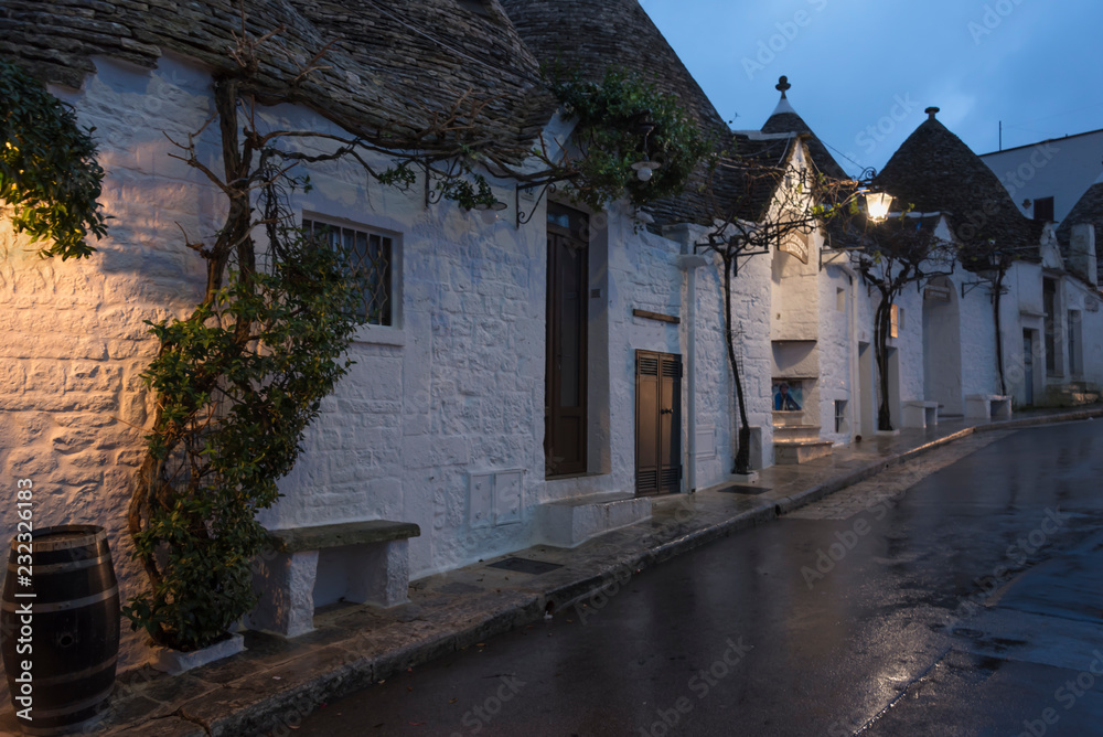 Traditional Trullo houses with conical roofs and wet pavement after rain in early morning.  Alberobe