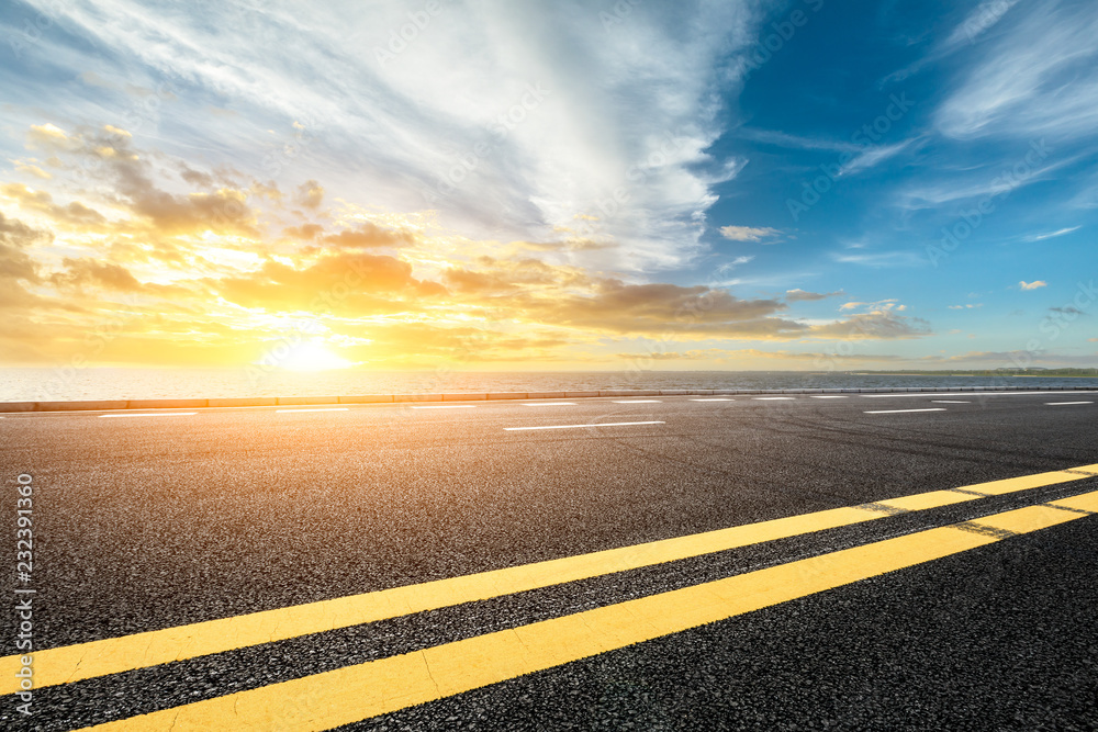 Asphalt road and dramatic sky with coastline at sunset