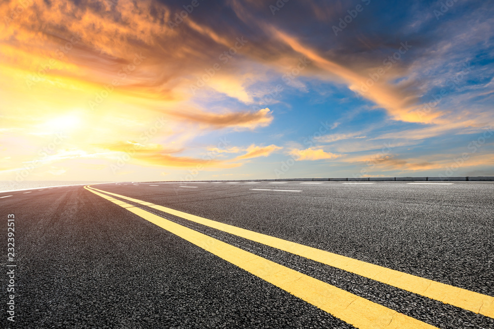 Asphalt road and dramatic sky with coastline at sunset