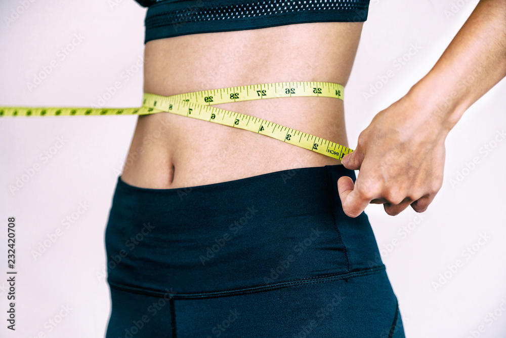 Close up shot of woman with slim body measuring her waistline and torso. Healthy nutrition and weigh