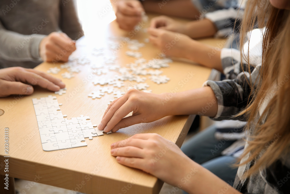 Group of people assembling puzzle on wooden table