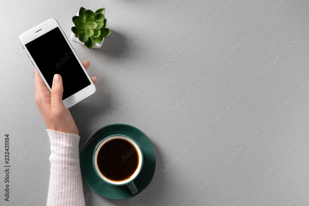 Female hand with mobile phone and cup of coffee on light background, top view