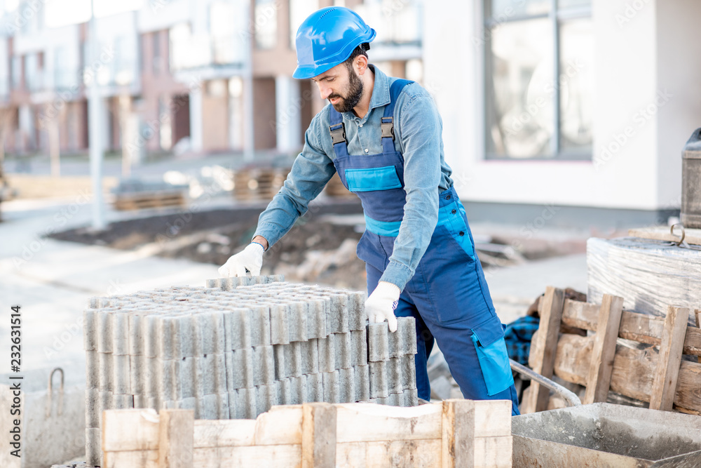 穿着制服的建筑工人从户外施工现场的托盘上取下铺路砖